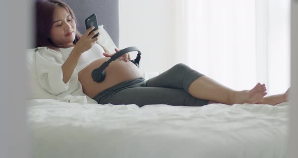 Young Asian pregnant wife turning on music for an unborn baby.