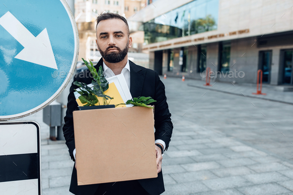 Depressed jobless person. Businessman standing with box of stuff outdoors near road sign, free space