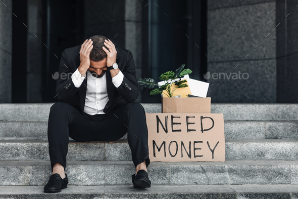 Unemployment concept. Disappointed middle-aged businessman sitting outdoors with placard and - Stock Photo - Images