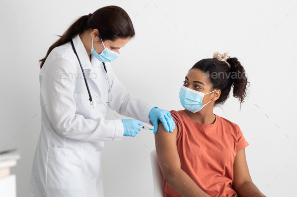 Nurse in white workwear making vaccination for black lady - Stock Photo - Images