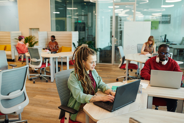 Bearded male office manager in casualwear using laptop against colleagues - Stock Photo - Images