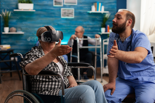 Male nurse giving social support, helping retired disabled senior woman to enjoy VR