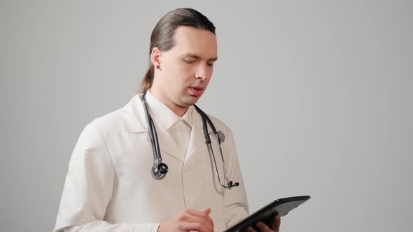 A Male Doctor with a Tablet in His Hands Advises the Patient About Treatment