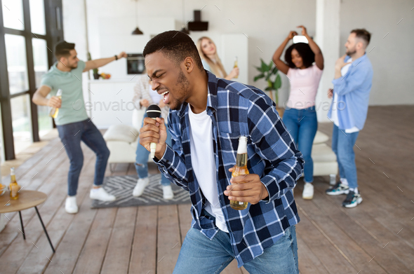 Emotional black guy with bottle of beer singing karaoke on student party with his international