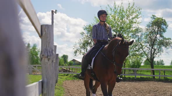 Female Jockey On A Brown Horse Riding Along The Wooden Fence In The Sandy Arena alt