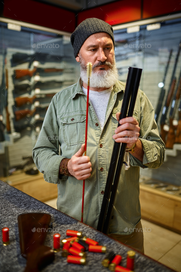 Bearded male hunter choosing ramrod in gun store
