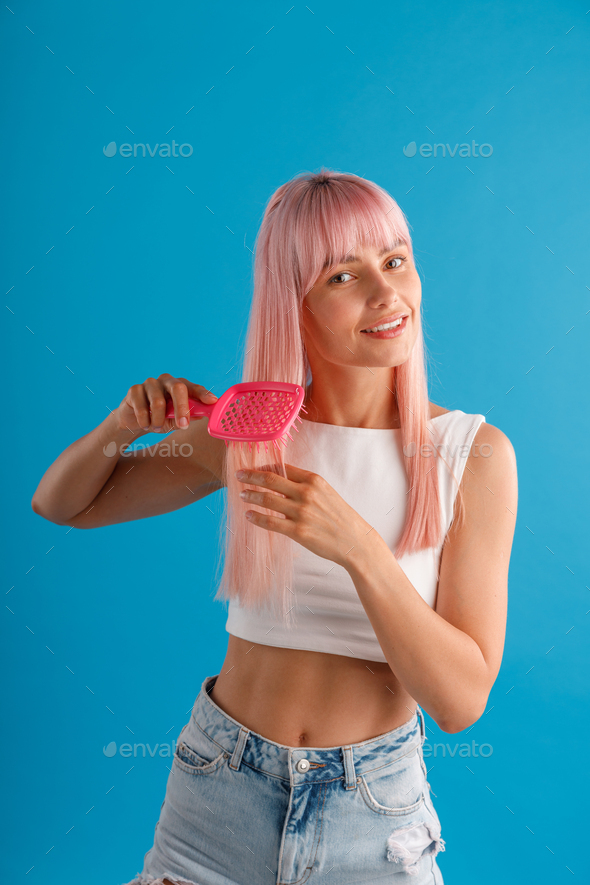 Smiling woman brushing her smooth natural long pink hair with hair comb while standing