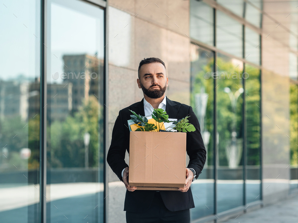 Man is upset by dismissal, lost his job. Fired male worker moving out office with box full of