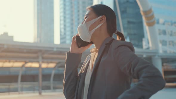 Asia businesswoman wear medical face mask talk via phone while walk alone outdoor.