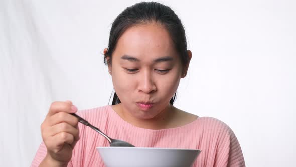 Asian woman eating cereales with milk on white background in studio. Woman having breakfast. alt