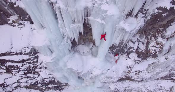 Aerial drone view of a man ice climbing on a frozen waterfall in the mountains. alt