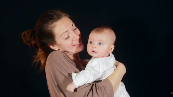 Mother Sings a Song To Her Child Holding Him in Her Arms on the Black Background