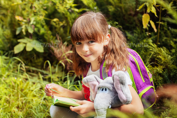 Little schoolgirl reads a book. A child with a backpack. Back to school. - Stock Photo - Images