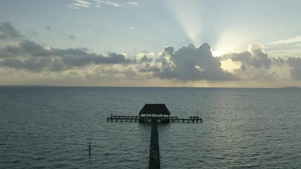 Aerial drone tilt up shot of sun rays through clouds over wooden pier on sea water in Mexico, North alt