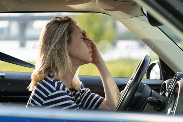 Unhappy tired female driver touch nose and forehead sitting in car driving suffering from headache