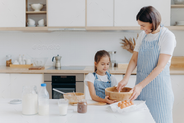 Beautiful stunning woman mother and daughter in aprons kitchen cooking in  the kitchen cookies and pasta noodles Stock Photo by ©marcink3333 169331726