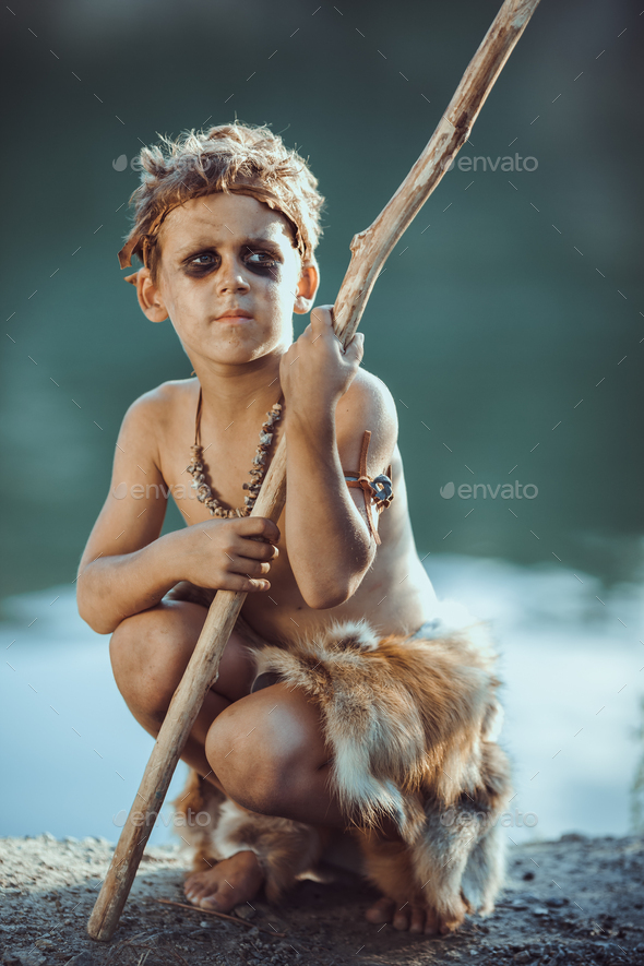 Cute caveman, manly boy with staff hunting outdoors. Ancient warrior