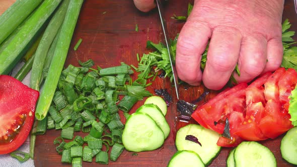 Slicing green parsley with a knife on a cutting board 