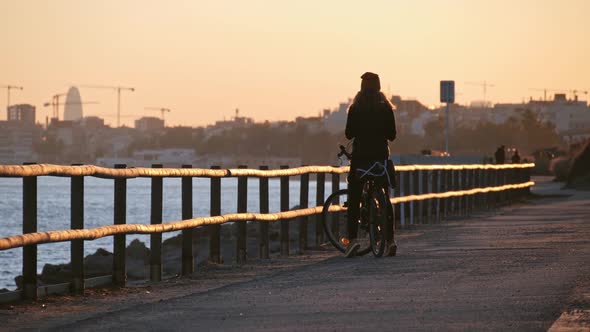 Girl with a Bicycle Standing at the Promenade Road at the Sunset