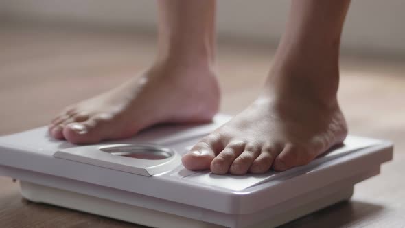 Close up of young Asian woman checking body weight on weighing scale in the living room at home.