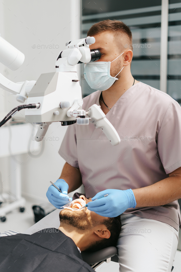 Male dentist wearing mask looking in the microscope