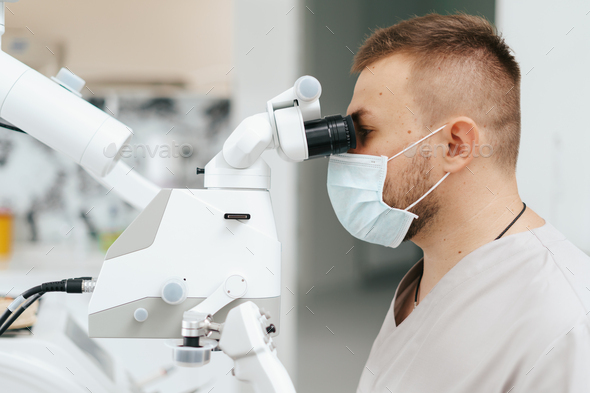 Male dentist wearing mask looking in the microscope
