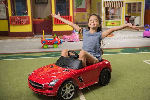 Happy little girl in toy car at game center. - Stock Photo - Images