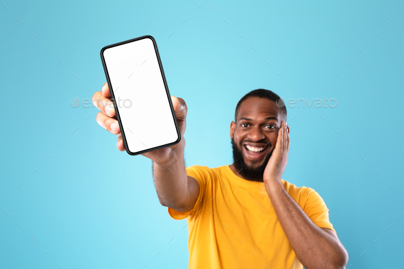 Excited black man presenting smartphone with empty screen, recommending website or ad, blue