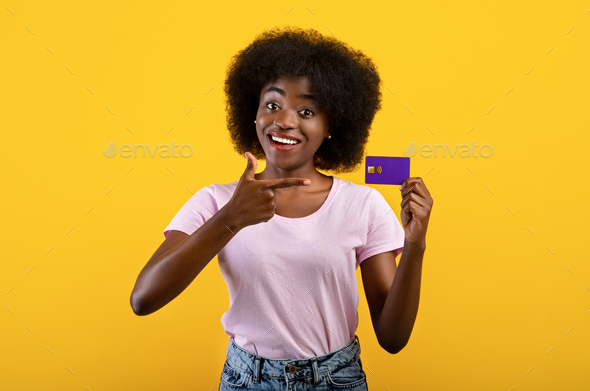 Positive african american bank customer showing credit card, recommending bank services, yellow