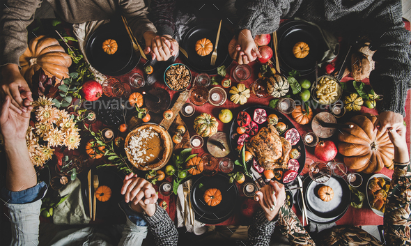 Family or friends praying holding hands at Thanksgiving celebration table