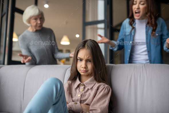 Upset daughter sitting on the couch, mom cursing.