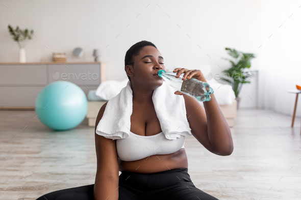 Wellness and slimming. Overweight black lady drinking clear sparkling water from bottle after