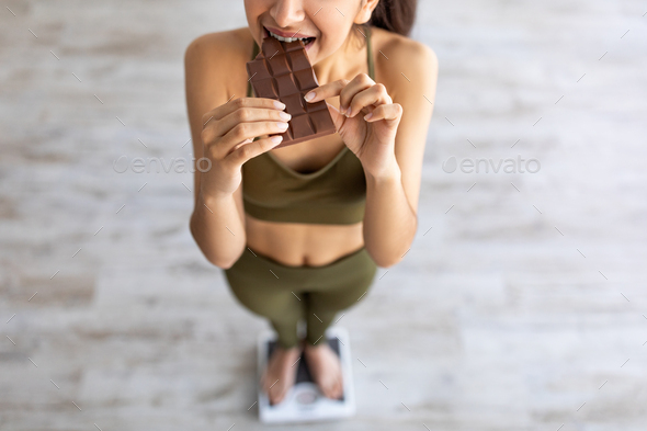 Diet failure, cheat meal concept. Above view of Indian woman eating chocolate while standing on
