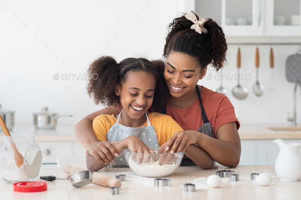 Black mother showing her teen daughter how to bake cookies