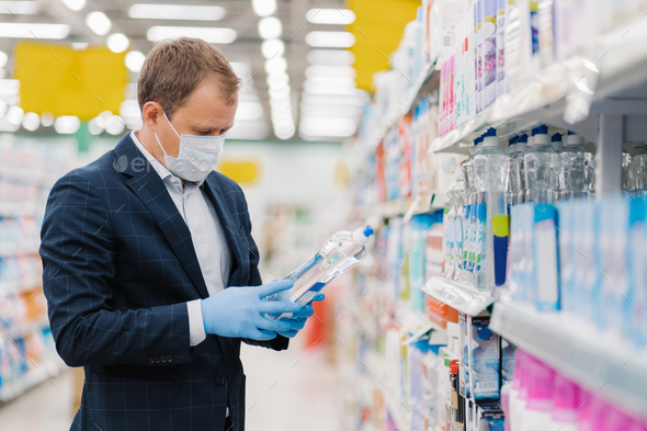 Man dressed in formal suit, covers mouth with medical mask, poses in supermarket