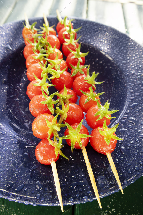 Skewer of red Pachino tomatoes over blue plate - Stock Photo - Images