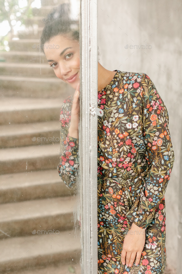 Portrait of smiling young black woman in dress with flowers pattern standing near glass