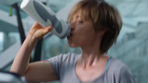 Woman Drinking Water while Running on Treadmill alt