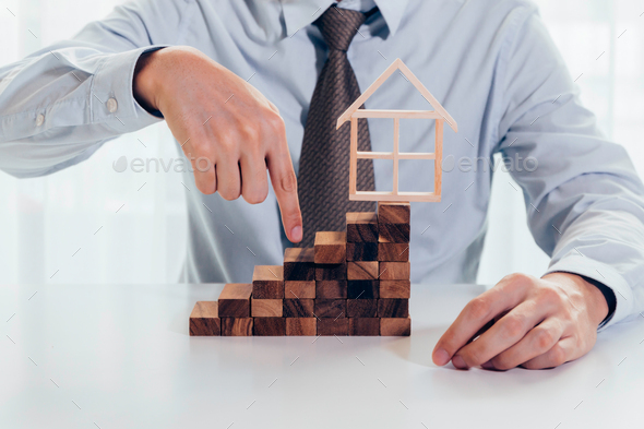 Close up of businessman using hand to climb up a stack of blocks towards house model