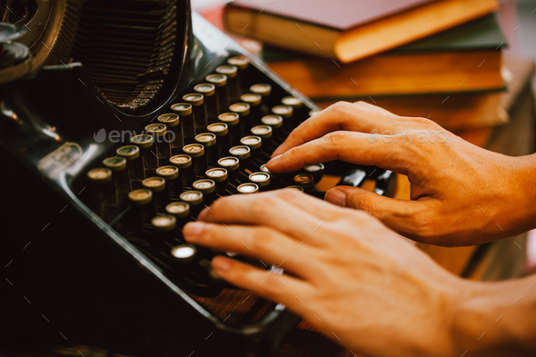 Human hands typing on vintage type writer machine and piles of books