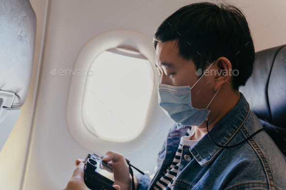 male tourist wearing a face mask inside aircraft cabin air and taking photos with a camera