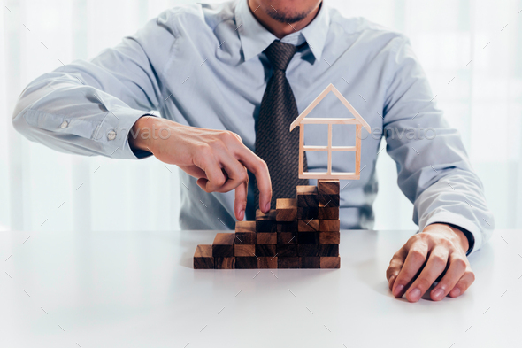 Close up of businessman using hand to climb up a stack of blocks towards house model