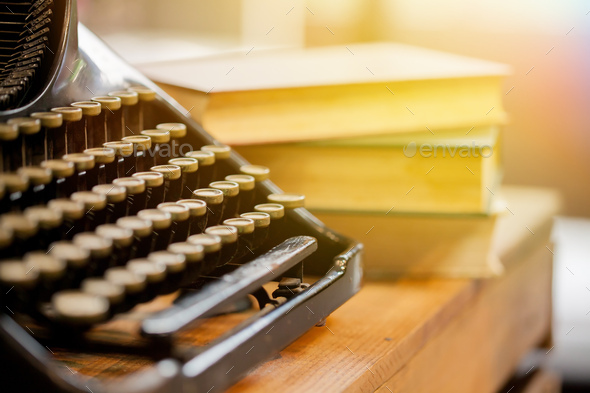 Old and vintage type writer machine and piles of books on wooden table - very selective focus