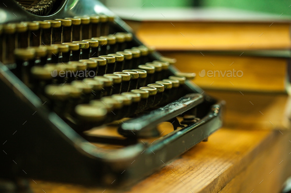 Old and vintage type writer machine and piles of books on wooden table - very selective focus.
