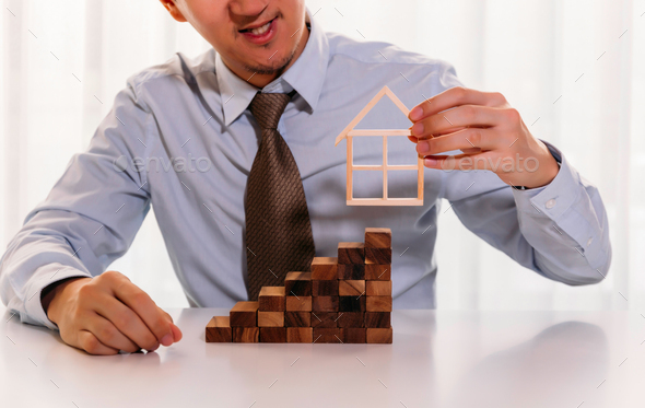 businessman putting on a house model on top of stack of blocks
