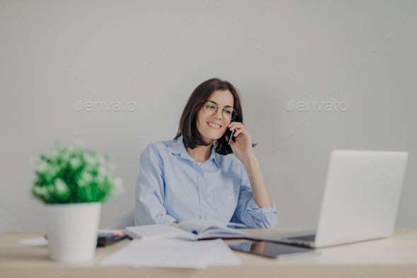 Beautiful female recruiter makes job offer to someone via phone, checks curriculum vitae on laptop - Stock Photo - Images