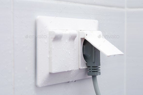 Weatherproof socket on a white tiled wall with water droplets.