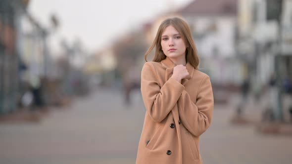 Attractive young lady in warm coat looking to camera on city street background alt