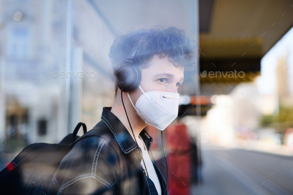 Portrait of young man commuter standing on bus stop outdoors in city, coronavirus concept