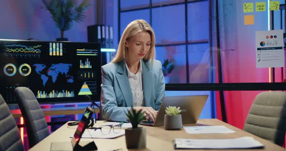 Businesswoman Working on Laptop and Making Important Notes Inot Paper Report in Evening Office alt